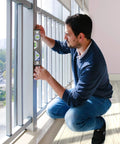 Man using Pro Grade Torpedo Level for precise alignment by window, demonstrating horizontal and vertical readings with 3 bubble vials.