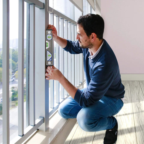 Man using Pro Grade Torpedo Level for precise alignment by window, demonstrating horizontal and vertical readings with 3 bubble vials.