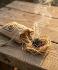 Smoldering tinder beside jute carry bag from Flint And Steel Fire Starter Kit With Hand Forged Carbon Steel Striker, English Flint Stone.