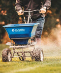 Person using Walk Behind Universal Spreader With 100 Lb Capacity For Seed Fertilizer Salt Ice Melt, 13 Inch Pneumatic Tires