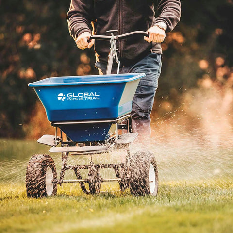 Person using Walk Behind Universal Spreader With 100 Lb Capacity For Seed Fertilizer Salt Ice Melt, 13 Inch Pneumatic Tires