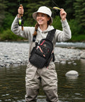 Woman fishing in river wearing Women's Fishing Sling Bag With Lure Rod Holder And Phone Pouch Waterproof 3600 Tackle Backpack With Removable Bait Binder Lightweight Convertible Gear Bag For Women Black.
