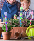 Two people arranging plants with colorful beaded garden stakes in a planter, featuring bright beads and decorative globes on top.