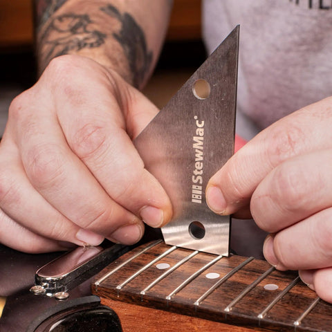 Hands use StewartMac guitar setup essentials with precision fret tool trio metric action gauge fret rocker and fret kisser for exact string height nut saddle and pickup alignment and fret diagnostics pro grade on electric guitar