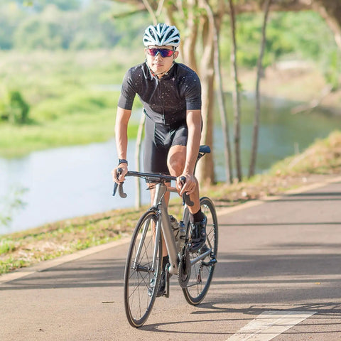 Cyclist riding on a road bike by a river, wearing a helmet and sunglasses, using 2 Pack 700C Bike Inner Tubes 18C 23C 25C With FV48mm Presta Valve