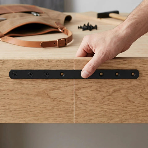 Hand holding Black Metal Joining Plates 4 Pcs Stainless Flat Straight Brackets With Screws on wooden panel for alignment