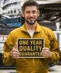 Mechanic in yellow jumpsuit holding sign 'One Year Quality Guarantee' in auto garage, emphasizing product reliability.
