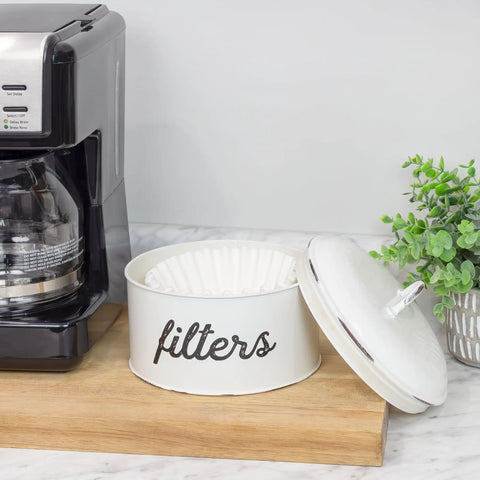 Basket Style White Enamel Coffee Filter Holder on kitchen counter, open with filters inside, next to coffee maker and plant.