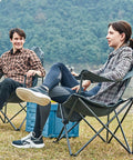 Two adults sitting in Oversized Folding Camping Chair With High Back Padded Comfort in a grassy field, black color.