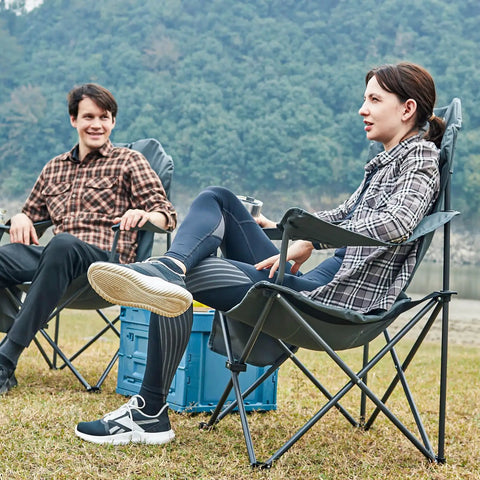 Two adults sitting in Oversized Folding Camping Chair With High Back Padded Comfort in a grassy field, black color.