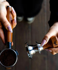 Hella Smooth Breville Espresso Accessories Kit With Bottomless Portafilter Plus Spring Loaded Tamper Featuring Rosewood Knock Box And Wdt Needle Distribution Station, showing hands holding portafilter and tamper.