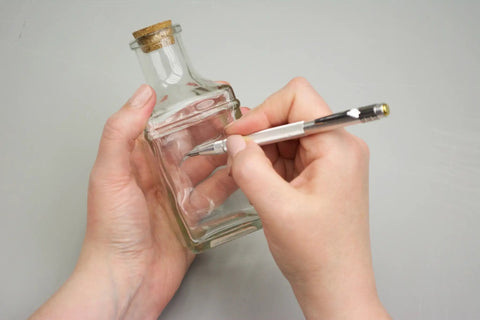 Person using Tungsten Carbide Scribe With Magnetic End And Replaceable Tip, Knurled Aluminum Handle to mark a glass bottle.