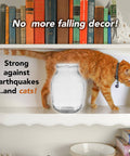 Cat walking on shelf with books beside clear vase secured with Clear Museum Gel Adhesive For Securing Collectibles And Decor Removable.