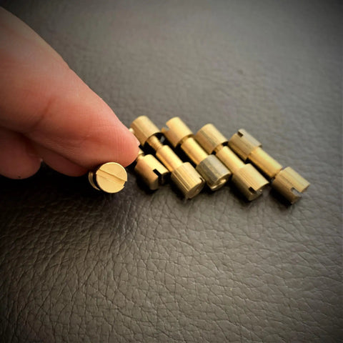 Hand holding a brass bolt from Knife Handle Making Brass Corby Bolts Pack of 6 for EDC DIY Builds with others lined up