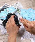 Lens cleaning tissue booklets (blue, 14) scattered around a camera lens being wiped.