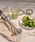 Heavy Duty Stainless Steel Immersion Blender With Kickass 600 Watt Motor And Turbo Switch on kitchen towel with green ingredients.