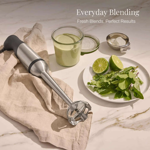 Heavy Duty Stainless Steel Immersion Blender With Kickass 600 Watt Motor And Turbo Switch on kitchen towel with green ingredients.