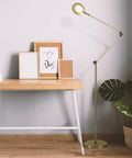 Sage 2 In 1 LED Craft Table And Floor Lamp Adjustable Floor Reading Light in gold finish beside wooden desk in living room.
