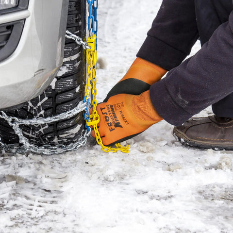 Person wearing waterproof insulated work gloves with thermal liner for cold weather, adjusting tire chains on snowy surface.