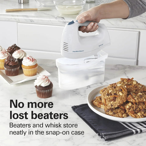 Hamilton Beach 6 Speed Electric Hand Mixer With Quick Burst And Bowl Rest Snap On Storage Case holding beaters near cupcakes and cookies.