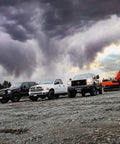 Three diesel trucks and an excavator under stormy clouds on gravel terrain