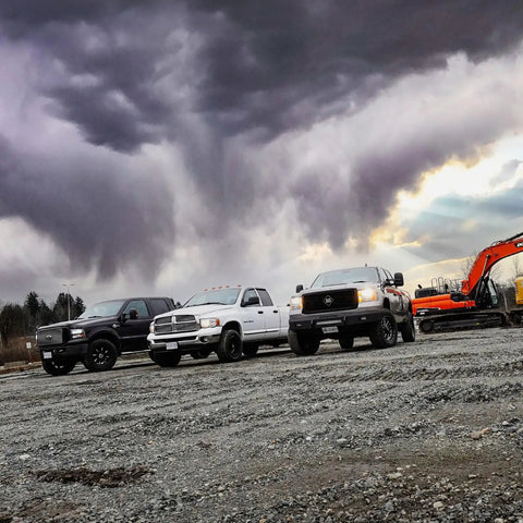 Three diesel trucks and an excavator under stormy clouds on gravel terrain