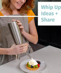 Person using 304 Stainless Steel Whipped Cream Dispenser 500ml With 3 Decorating Nozzles on dessert in kitchen.