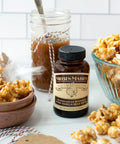 Jar of Madagascar Bourbon Pure Vanilla Bean Paste surrounded by caramel popcorn and sauce jar on kitchen counter
