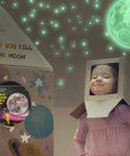 Child in cardboard rocket under glow in the dark ceiling stars and moon wall decals for kids bedroom or nursery, green glow effect