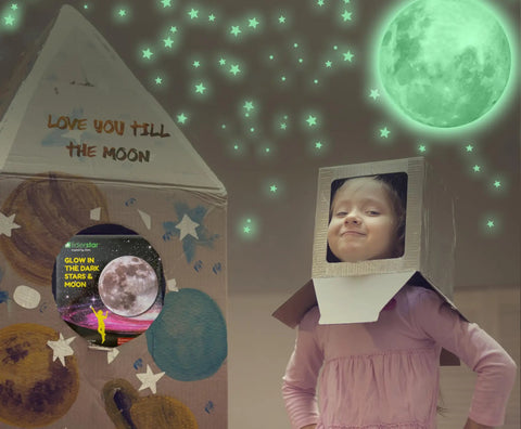 Child in cardboard rocket under glow in the dark ceiling stars and moon wall decals for kids bedroom or nursery, green glow effect