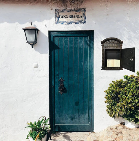 Image of Outdoor Metal Wall Mounted Mailbox with vintage cast iron locking look and old school charm next to a blue door on a white wall.