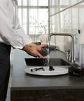 Person cleaning components of the Dinamica Plus Fully Automatic Espresso Machine With Built In Grinder And Auto Milk Frother in a kitchen sink.