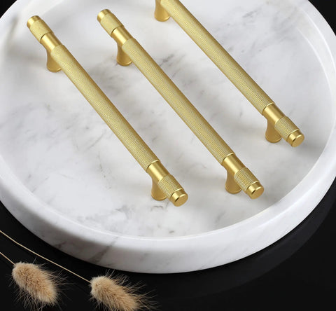 Ten Pack Gold Knurled Cabinet Pulls With 5 Inch Hole Centers 7 Inch Overall Length Brushed Brass Handles on marble surface.