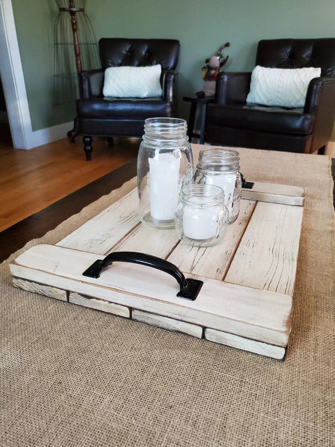 Rustic wooden tray with black handles, mason jar candles, and brown furniture in background.