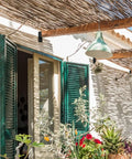 Outdoor patio with green shutters, hanging light fixture, and natural wooden pergola providing shade.