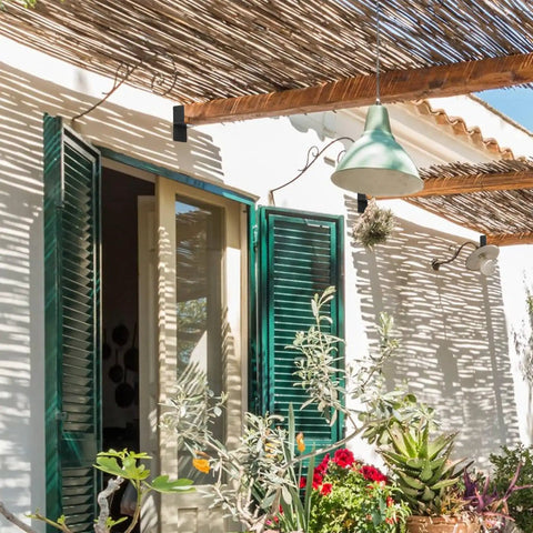 Outdoor patio with green shutters, hanging light fixture, and natural wooden pergola providing shade.
