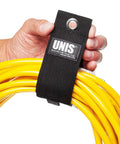 Hand holding yellow cables secured with black 8 Pack Heavy Duty Large 13 Inch Extension Cord Organizer Straps with hang loop.