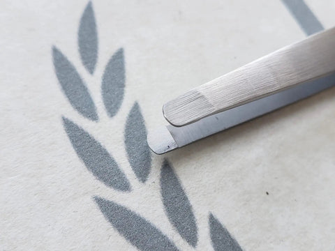 Round Tip Tweezer For Men Premium Stainless Steel Eyebrow And Facial Hair Remover Made In USA Precision Grooming Tool With Superior Alignment And Detailed 40 Step Finish That Elevates Your Brow Game And Makes Clean Easy Brow Shaping. close-up of round tip stainless steel tweezer on paper