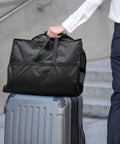 Person holding On The Go Travel Garment Bag 43 Inch Heavy Duty Suit Carrier With Zipper Pocket on top of suitcase, black color