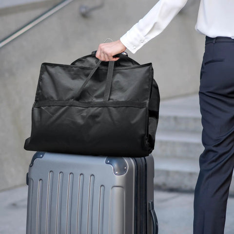 Person holding On The Go Travel Garment Bag 43 Inch Heavy Duty Suit Carrier With Zipper Pocket on top of suitcase, black color