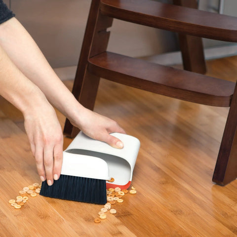 Compact Dustpan And Brush Set With Snap In Design And Bristle Cover used on hardwood floor under chair