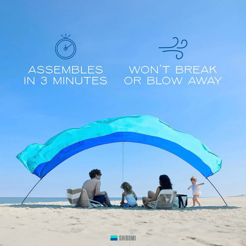 World's Best Beach Shade Wind Powered Shelter for the beach, lightweight 4 lb, easy setup, accommodating a beach group under blue sky.