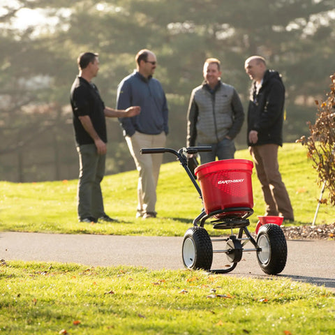 Heavy Duty 50 Lb Broadcast Fertilizer Spreader For Lawns on grass with 13-inch pneumatic tires, men talking in background