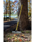 Heavy-Duty 55-Inch Fiberglass Rake With A 21-Inch Steel Tined Head For De-Thatching And Landscaping leaning against a tree