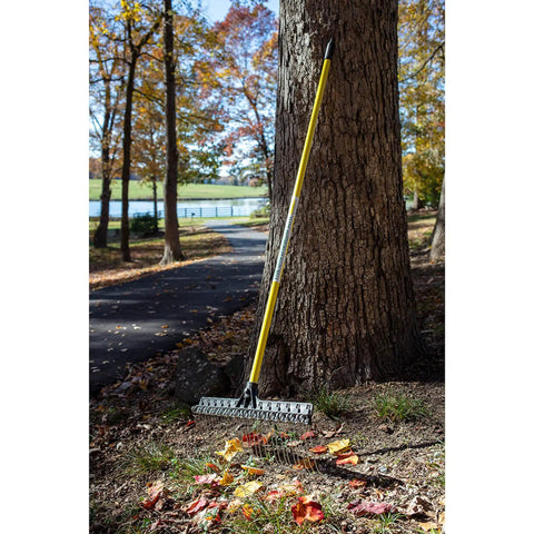Heavy-Duty 55-Inch Fiberglass Rake With A 21-Inch Steel Tined Head For De-Thatching And Landscaping leaning against a tree