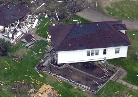 Aerial view of a damaged house lifted from its foundation after a natural disaster, debris scattered around the structure.