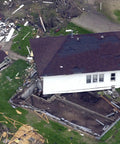 An aerial view of a damaged house split in half after a natural disaster, showing debris and destruction around the neighborhood.