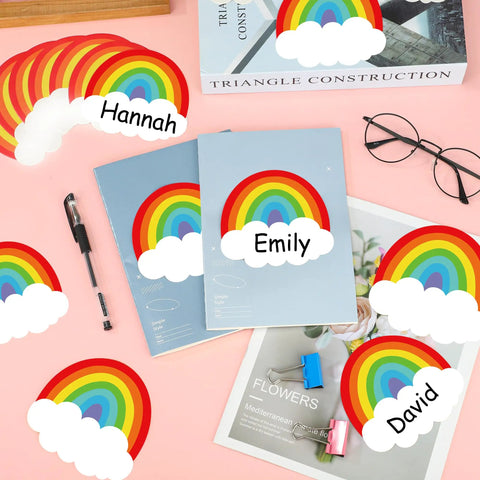 Colorful 120 Rainbow Name Plates For Classroom Desks with self-adhesive backing displayed on pink desk with supplies and books.