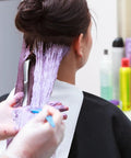 Hairdresser applying purple hair dye to woman's hair in salon with hair products in background
