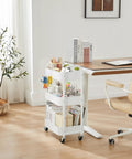 White 3-Tier Rolling Utility Cart With Caster Wheels For Kitchen And Bath next to desk, holds books and stationery.